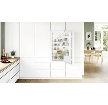 Réfrigérateur encastrable Bosch dans une cuisine moderne et lumineuse avec des façades blanches et des étagères intérieures.
