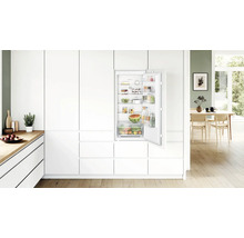 Réfrigérateur encastrable Bosch intégré dans une cuisine moderne blanche avec porte ouverte et étagères remplies.