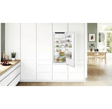 Réfrigérateur encastrable dans une cuisine moderne blanche avec porte ouverte, rempli d'aliments frais et logo Bosch.