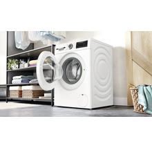 Lave-linge séchant Bosch dans une buanderie lumineuse avec porte ouverte, à côté d'une étagère avec des serviettes et un panier à linge.