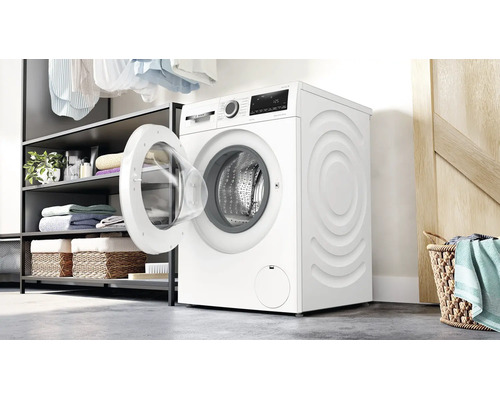 Lave-linge séchant Bosch dans une buanderie lumineuse avec porte ouverte, à côté d'une étagère avec des serviettes et un panier à linge.
