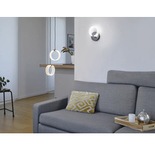 Modernes Wohnzimmer mit ringförmigen LED Pendelleuchten und passender Wandleuchte über einem grauen Sofa.