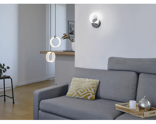 Modernes Wohnzimmer mit ringförmigen LED Pendelleuchten und passender Wandleuchte über einem grauen Sofa.