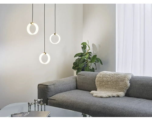Drei moderne, ringförmige Pendelleuchten hängen über einem grauen Sofa mit Fellauflage in einem hellen, stilvoll eingerichteten Wohnzimmer.