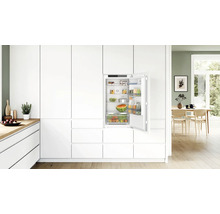 Réfrigérateur encastrable Bosch intégré dans une cuisine moderne blanche avec porte ouverte et étagères remplies.