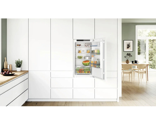 Réfrigérateur encastrable Bosch intégré dans une cuisine moderne blanche avec porte ouverte et étagères remplies.