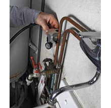 Hand legt Thermometer an Kupferrohr einer Wasserinstallation mit Mischbatterie und Absperrventil