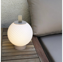 Moderne runde LED Tischleuchte fuer den Aussenbereich mit Trageschlaufe auf einem Holztisch neben einem Polster.