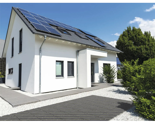 Maison individuelle moderne avec panneaux solaires sur le toit et aménagement extérieur soigné avec chemin pavé et gravier.