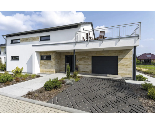 Maison individuelle moderne avec revêtement en pierre naturelle, garage, balcon avec garde-corps en acier inoxydable et allée pavée décorative.