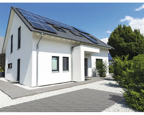 Maison individuelle avec panneaux solaires sur le toit et jardin moderne aménagé avec allée pavée et lit de gravier.