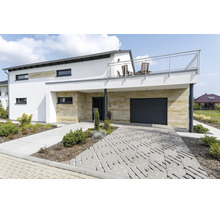 Maison individuelle moderne avec revêtement en pierre naturelle, garage, balcon et pavage en dalles gazon dans le jardin devant.