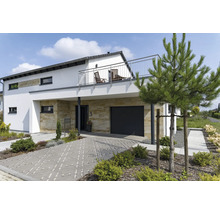 Maison moderne avec revêtement en pierre naturelle au rez-de-chaussée, garage, balcon avec garde-corps en acier inoxydable et allée pavée.