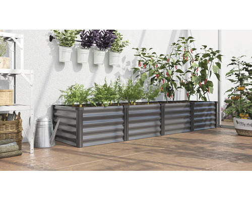 Rechteckiges Hochbeet aus Metall in einem Gewächshaus mit verschiedenen Pflanzen wie Paprika und Karotten auf einem Terrassenboden.