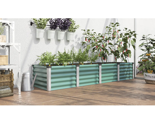 Un potager surélevé rectangulaire en métal dans une serre avec diverses plantes, herbes et légumes.