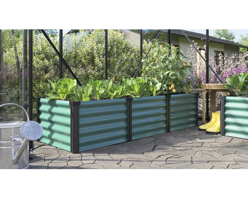 Potager surélevé rectangulaire en métal avec structure ondulée dans une serre avec des plantes et des outils de jardin sur une terrasse.