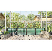 Grand bac à plantes surélevé en métal dans une serre avec des plants de tomates sur une terrasse en bois avec arrosoir et caisses en bois.