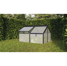 Une petite serre avec cadre en aluminium et panneaux alvéolaires installée dans un jardin devant une haie.