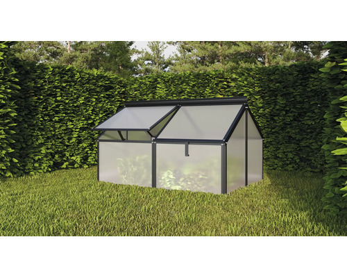 Une petite serre avec cadre en aluminium et panneaux alvéolaires installée dans un jardin devant une haie.