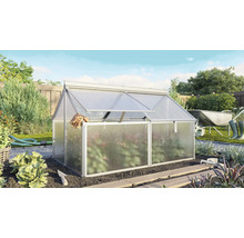 Châssis de forçage en aluminium avec plaques alvéolaires dans un jardin ensoleillé avec des outils de jardinage et des plantes en arrière-plan.