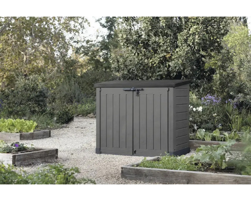 Coffre de jardin en plastique avec double porte pour rangement dans le jardin posé sur une allée de gravier devant des plates bandes