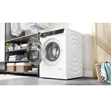 Un lave linge Bosch est installe dans une buanderie lumineuse a cote d une etagere avec des serviettes et un panier a linge.