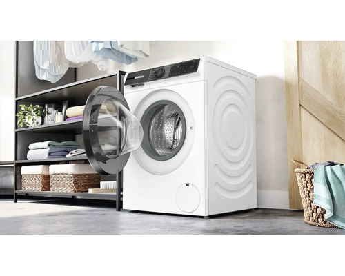 Un lave linge Bosch est installe dans une buanderie lumineuse a cote d une etagere avec des serviettes et un panier a linge.