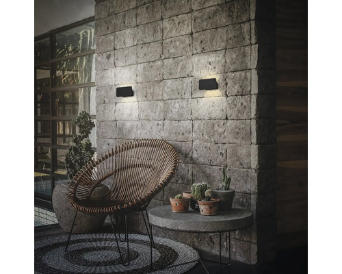 Moderne rechteckige LED Wandleuchten montiert an einer Natursteinmauer über einem Sitzbereich mit Rattan Sessel und Beistelltisch.