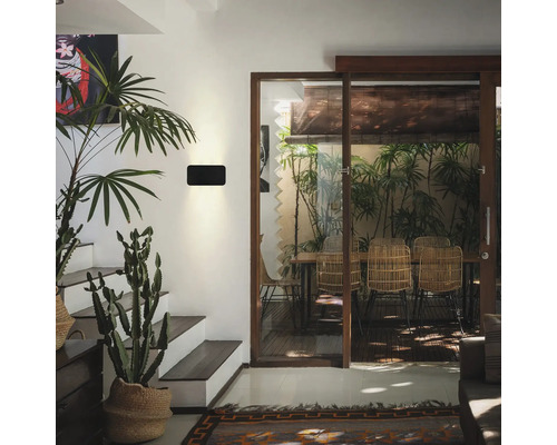 Moderne Wandleuchte in einem hellen Wohnraum mit Treppe und Blick auf eine Terrasse mit Rattanmöbeln.
