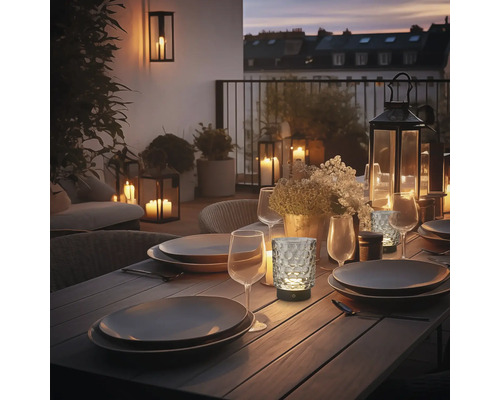 LED Tischleuchte in Windlicht Optik mit strukturiertem Glas auf einem gedeckten Terrassentisch bei Abenddämmerung.