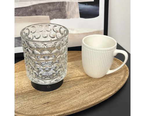Eine strukturierte Glaslampe mit schwarzem Sockel und Ein Aus Schalter neben einer gerippten Tasse auf einem ovalen Holztablett.
