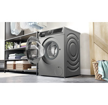 Un lave-linge pose libre avec porte ouverte dans une buanderie avec des étagères et un panier à linge.