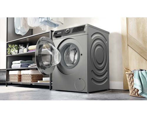 Un lave-linge pose libre avec porte ouverte dans une buanderie avec des étagères et un panier à linge.