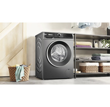 Un lave-linge Bosch est installé dans une buanderie moderne à côté d'une étagère à linge et d'un panier en osier.