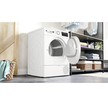 Sèche-linge Bosch en pose libre, porte ouverte, dans une buanderie moderne avec étagères et panier à linge.