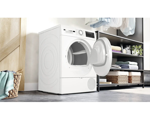 Sèche-linge Bosch en pose libre, porte ouverte, dans une buanderie moderne avec étagères et panier à linge.