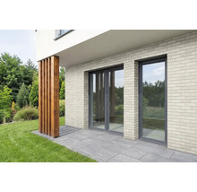 Moderne Hausfassade mit Klinkerriemchen, bodentiefen Fenstern und einer Holzstütze auf einer Terrasse vor einer Gartenlandschaft.
