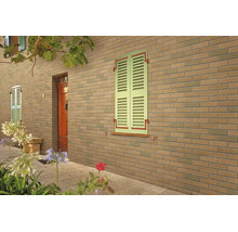 Fassadenansicht eines Hauses mit Ziegelmauerwerk und Fensterlaeden an einer Steinmauer neben einer Eingangstuer.
