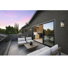 Moderne Dachterrasse mit Lounge Mobiliar, Steinfliesen und Schiebetür zum Wohnbereich in einem Haus mit dunkler Ziegelfassade bei Dämmerung.