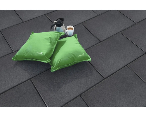 Dalles de terrasse rectangulaires sombres avec deux coussins verts, une cafetière et une tasse de café posées sur une surface plane.