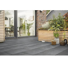 Terrasse moderne avec grand dallage en grès cérame, bordée d'une façade en bois avec jardinière surélevée et baies vitrées toute hauteur.