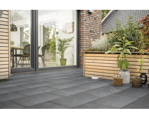 Terrasse moderne avec grand dallage en grès cérame, bordée d'une façade en bois avec jardinière surélevée et baies vitrées toute hauteur.