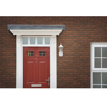 Eingangsbereich eines Hauses mit roter Haustür, weißem Türrahmen und Wandlampe an einer Ziegelfassade.