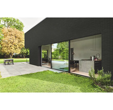 Modernes Wohnhaus mit dunkler Ziegelfassade, grosser Glasfront zur Terrasse und Blick auf eine offene Küche mit Kochinsel im Gartenbereich.