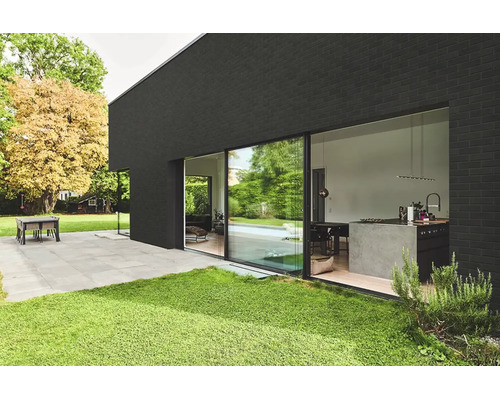 Moderne schwarze Hausfassade mit großen Schiebetüren und Blick in ein offenes Wohnkonzept mit Küche und Terrasse im Garten.