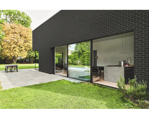 Modernes Wohnhaus mit dunkler Ziegelfassade und großen Schiebetüren zur Terrasse mit Gartenbereich.