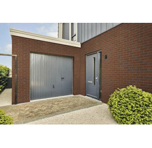 Moderne Hausfassade mit Klinkerriemchen, Garagentor und Eingangstür in einem Außenbereich mit Pflasterung.