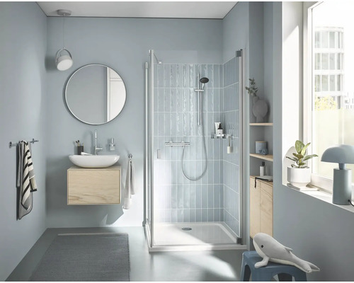 Modernes Badezimmer mit Dusche mit Glastür und Duscharmatur, wandhängendem Waschtisch, rundem Spiegel und gefliesten Wänden in heller Gestaltung.