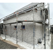Ein Wohnhaus mit gemauerter Fassade, das für Renovierungsarbeiten mit einem Metallgerüst umbaut ist.