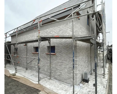 Ein Wohnhaus mit gemauerter Fassade, das für Renovierungsarbeiten mit einem Metallgerüst umbaut ist.